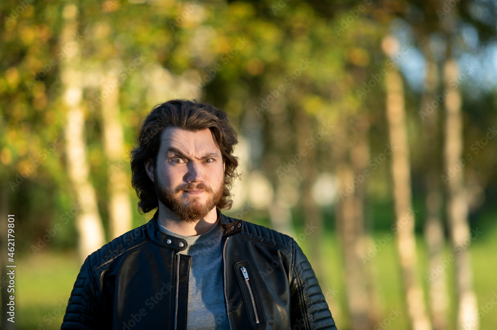Young bearded man standing and looking at camera against a background of colorful autumn trees Young bearded man standing and looking at camera against a background of colorful autumn trees
