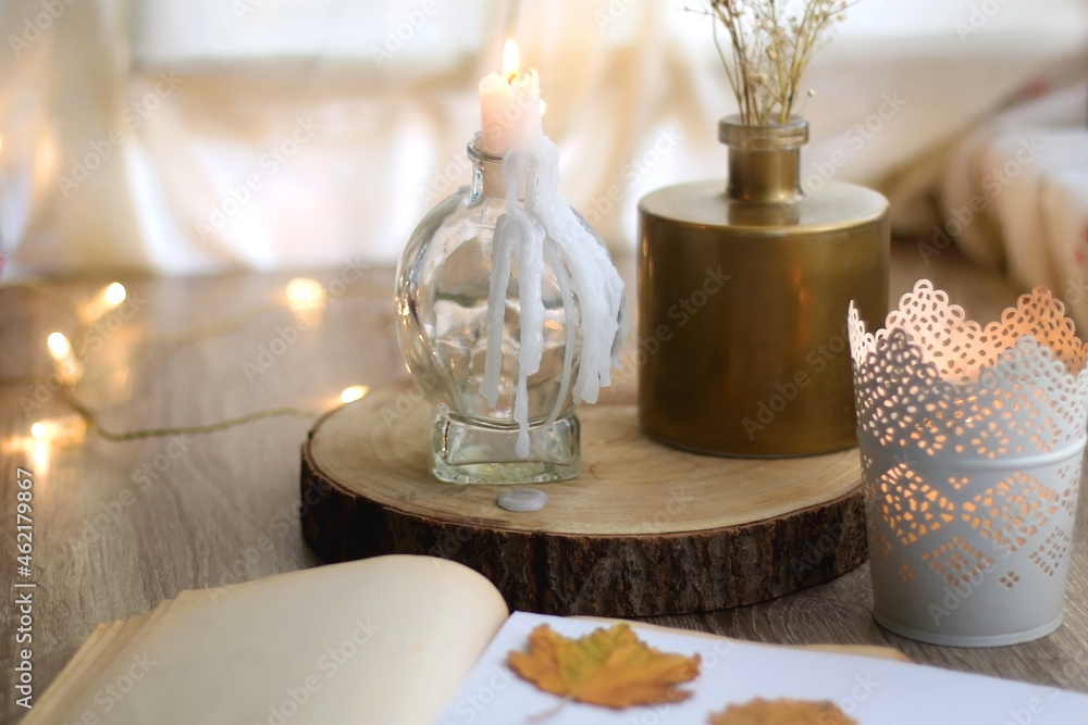 Old book with pressed autumn leaves, lit candles and vase with gypsophila flowers. Selective focus.