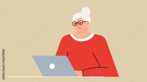Senior woman studies and studies modern technologies using a laptop. A positive smiling grandmother sits at a computer, communicates on the Internet online and learns new things. An adult is working.