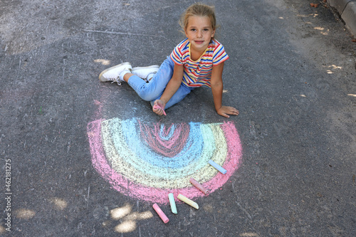 Cute little child drawing rainbow with colorful chalk on asphalt