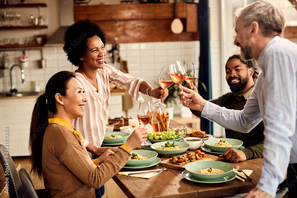 Group of happy multi-ethnic friends celebrate and toast with wine at dining table.