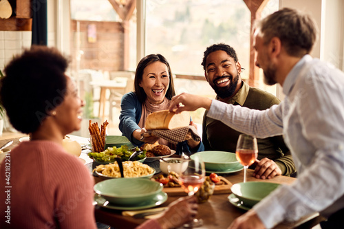 Happy multi-ethnic friends have fun while eating together at dining table.