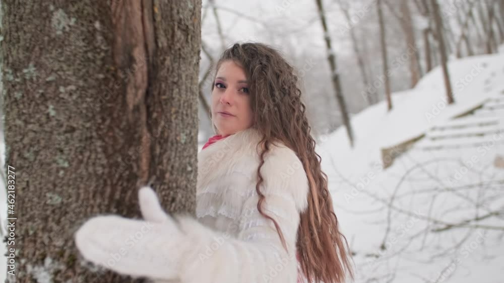 Young woman walking in winter park. Happy woman enjoys nature. Woman in white jacket and red scarf. Tracking shot of cute female walks outdoors. 4K, UHD