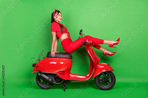 Full length body size photo smiling woman in red clothes sitting on motorbike isolated vibrant green color background