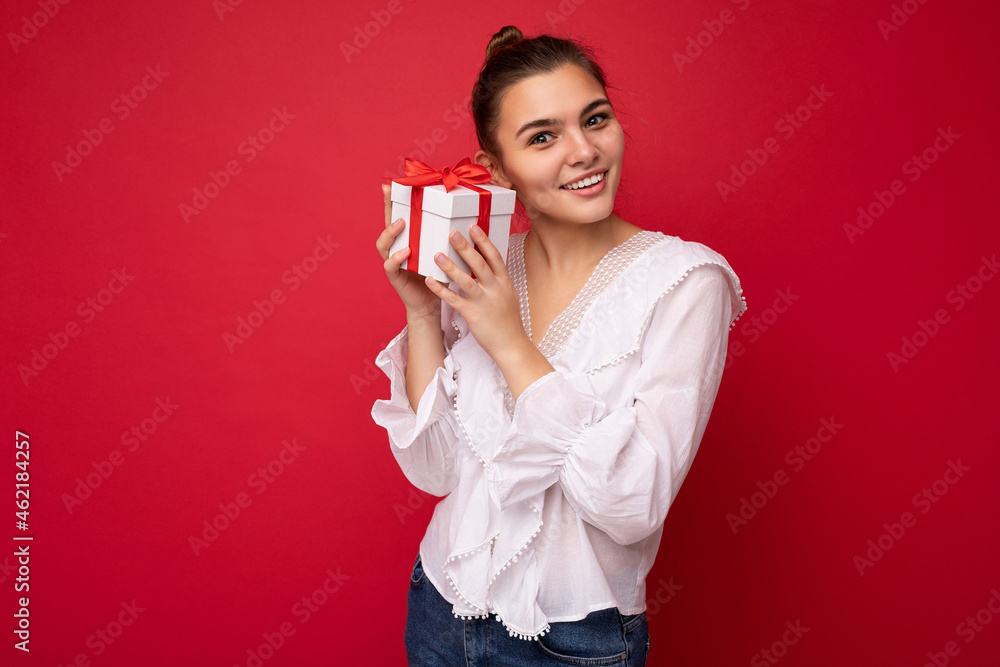 Beautiful happy young brunette woman isolated over colourful background wall wearing stylish casual clothes holding gift box and looking at camera Beautiful happy young brunette woman isolated over colourful background wall wearing stylish casual clothes holding gift box and looking at camera