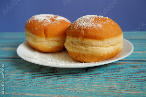 two doughnuts , sprinkled with powdered sugar , on a white plate on a blue wooden background 