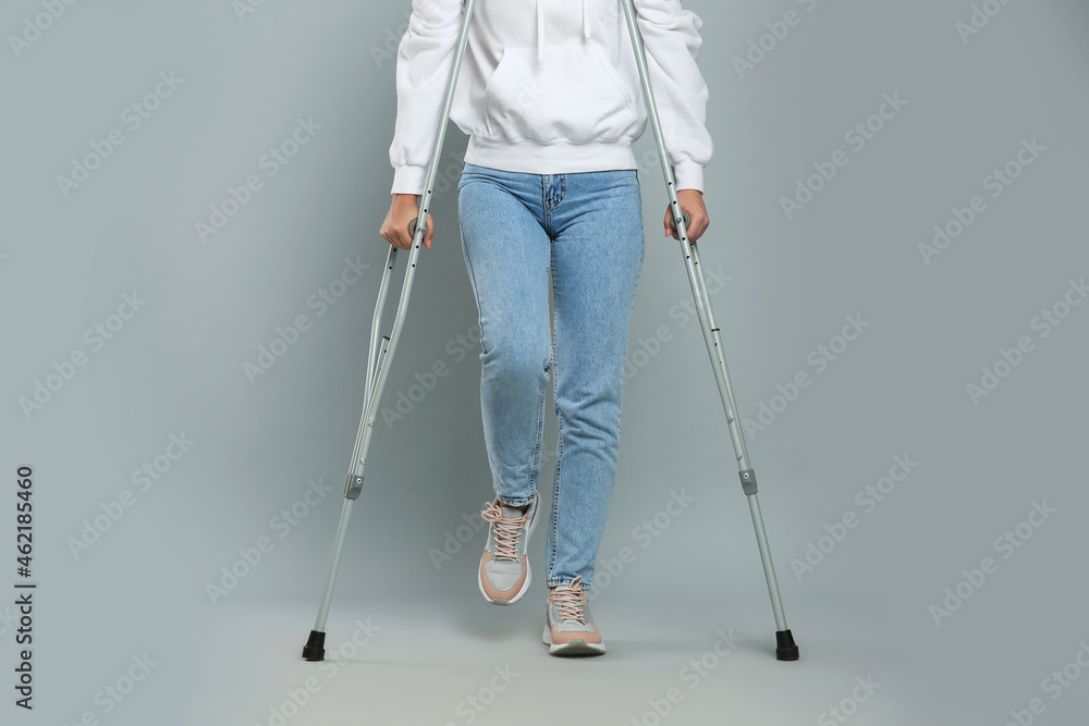 Young woman with axillary crutches on grey background, closeup Young woman with axillary crutches on grey background, closeup