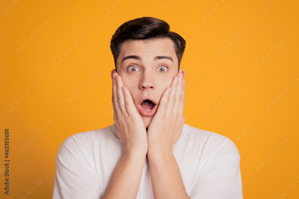 Photo of astonished young man open mouth put hands face isolated on yellow background Photo of astonished young man open mouth put hands face isolated on yellow background