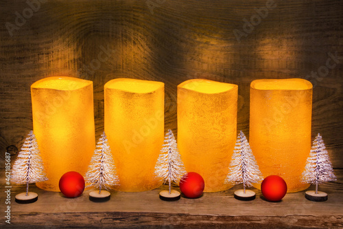 4 golden electric LED wax candles and Christmas decoration on wooden background photo