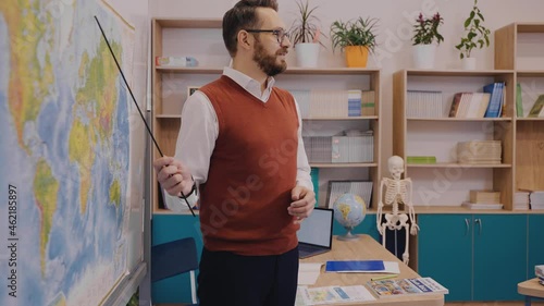 Positive male teacher standing at the world map and explaining a topic in geography. Male teacher showing the world map. Modern school with excited and progressive teacher. High quality 4k footage