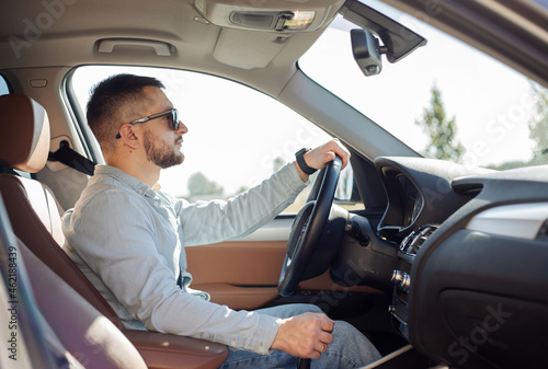 Handsome young man in smart casual wear driving a status car.