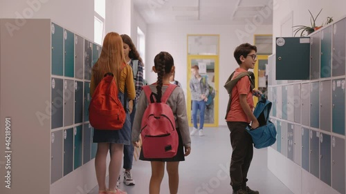 Children walk in school hall, boy closes his locker. Modern school corridor at break. Girl walking down the school hallway. Bright and modern school. High quality 4k footage