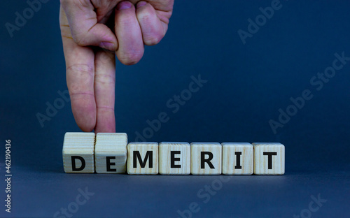Demerit or merit symbol. Businessman turns wooden cubes and changes words 'demerit' to 'merit'. Beautiful grey table, grey background, copy space. Business and demerit or merit concept.