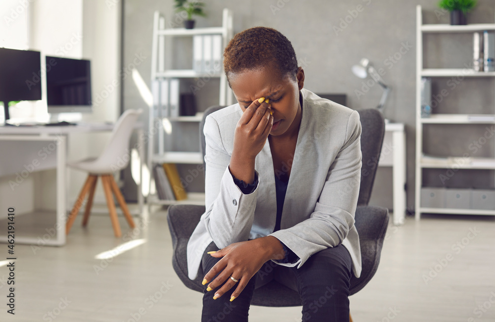 Exhausted and frustrated woman is working on difficult business task and has bad conversation. Tired african american young female company manager sitting in office in front of webcam and rubbing eyes - obrazy, fototapety, plakaty 