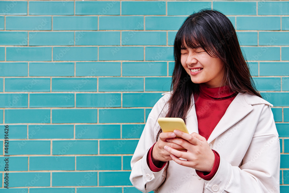 Woman with eyes closed holding smart phone in front of turquoise wall Woman with eyes closed holding smart phone in front of turquoise wall