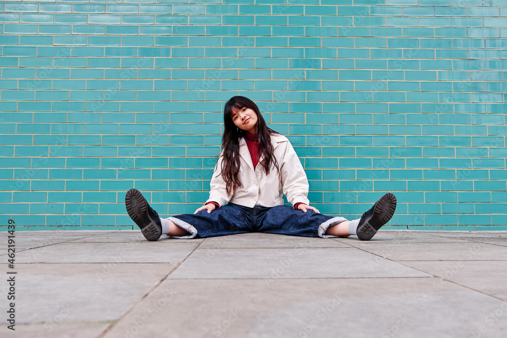 Beautiful young woman sitting with legs apart in front of brick wall Beautiful young woman sitting with legs apart in front of brick wall