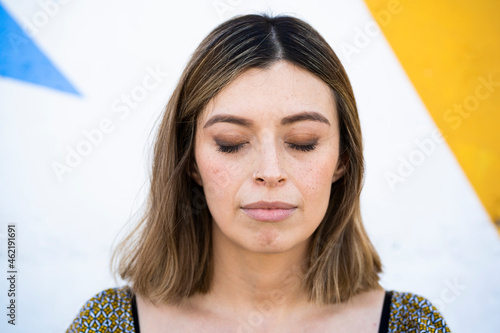 Young woman with eyes closed in front of wall photo