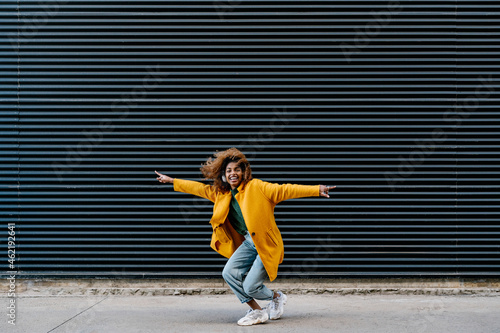 Cheerful Afro woman with arms outstretched having fun against wall photo