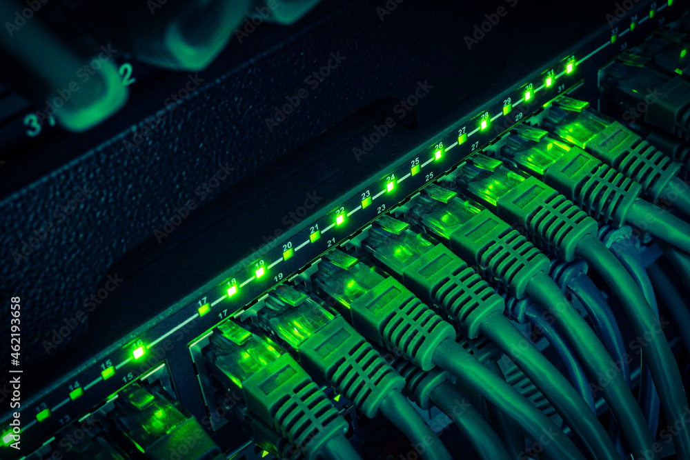 Close up of green network cables from data center connected with patch cord to black switch glowing in the dark