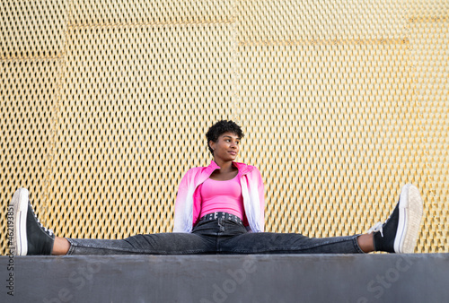 Young woman looking away while sitting with spreading legs by wall photo