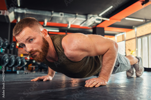 Fototapeta Naklejka Na Ścianę i Meble -  Portrait of young bearded athletic man doing push-ups in the gym. Close-up. The concept of fitness and training
