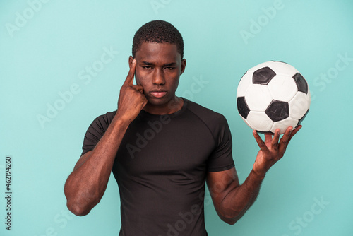 Young African American man playing football isolated on blue background pointing temple with finger, thinking, focused on a task.