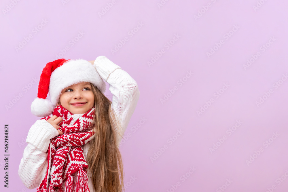 A little smiling girl in a New Year's hat and a warm Christmas scarf on an isolated background.