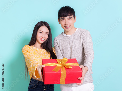 Happy young couple showing gift.Isolated on blue background.