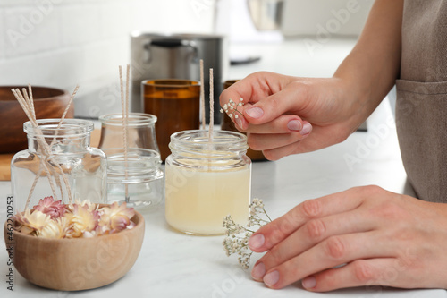Fotografija Woman decorating homemade candle with gypsophila flowers at table indoors, close