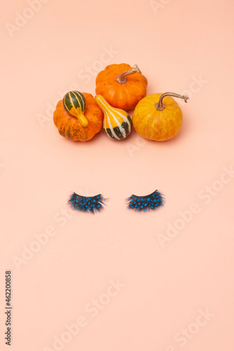 Creative woman face made of eyelashes and pumpkins hair on the orange background. Minimal beauty concept. Flat lay. Helloween makeup creative concept.