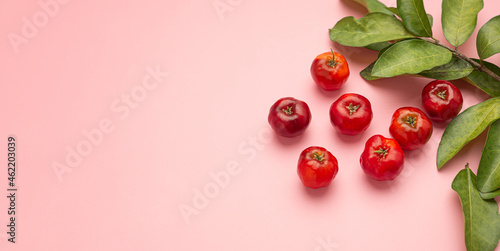 Ripe red acerola cherries fruit and green leaves isolated on a pink background. High vitamin C and antioxidant fruits. Top view. Flat lay. Space for text. Concept of healthy fruits photo