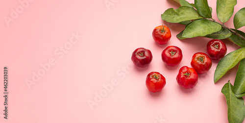 Foto Ripe red acerola cherries fruit and green leaves isolated on a pink background