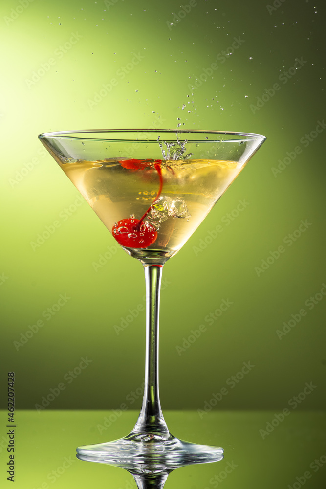 cocktail martini with cherries and splash with splashes in a glass on a green background cocktail martini with cherries and splash with splashes in a glass on a green background
