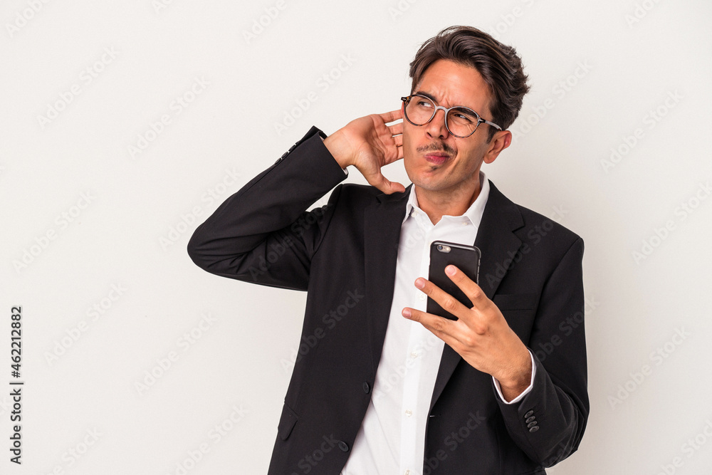 Young mixed race business man holding mobile phone isolated on white background touching back of head, thinking and making a choice. Young mixed race business man holding mobile phone isolated on white background touching back of head, thinking and making a choice.
