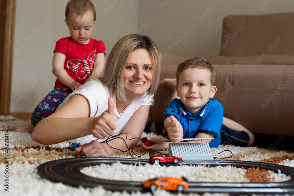 Mom and son play racing on the carpet, and the little daughter sits on her mother's back. Mom and son play racing on the carpet, and the little daughter sits on her mother's back.