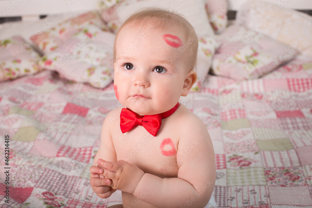 Image of adorable child with red kisses on the skin, happy boy, sitting in the Studio on the bed, angel, romantic holiday, Valentine's Day. Image of adorable child with red kisses on the skin, happy boy, sitting in the Studio on the bed, angel, romantic holiday, Valentine's Day.