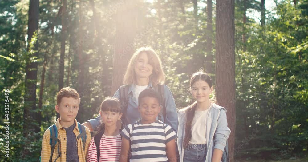 Waist up portrait of the cute children posing at the forest while spending time at the camping with their female couch or teacher at the nature. Happy childhood concept Waist up portrait of the cute children posing at the forest while spending time at the camping with their female couch or teacher at the nature. Happy childhood concept