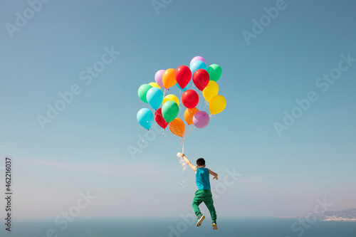 Boy flying with bunch of balloons in sky