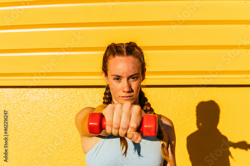 Sportswoman holding dumbbell in front of yellow wall photo