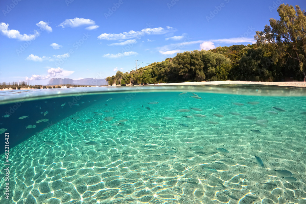 Beautiful underwater split above and below photo of rocky seascape with deep blue sky and clouds and rich marine life in tropical exotic island destination