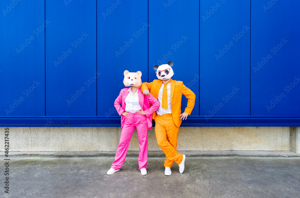 Man and woman wearing vibrant suits and bear masks standing together against blue wall Man and woman wearing vibrant suits and bear masks standing together against blue wall