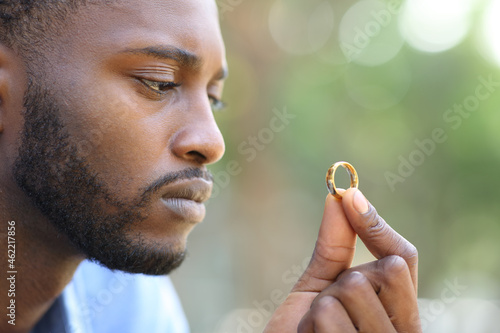 Sad black husband doubting holding wedding ring photo