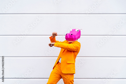 Man wearing vibrant orange suit and hippo mask dancing in front of white wall photo