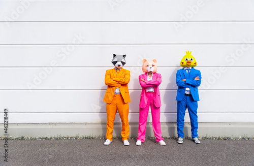 Three people wearing vibrant suits and animal masks posing side by side in front of white wall
