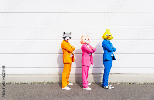 Three people wearing vibrant suits and animal masks posing side by side in front of white wall photo