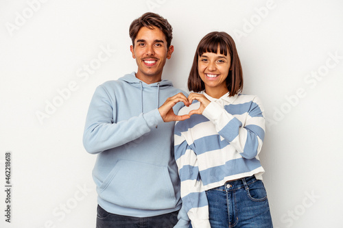 Young mixed race couple isolated on white background smiling and showing a heart shape with hands.