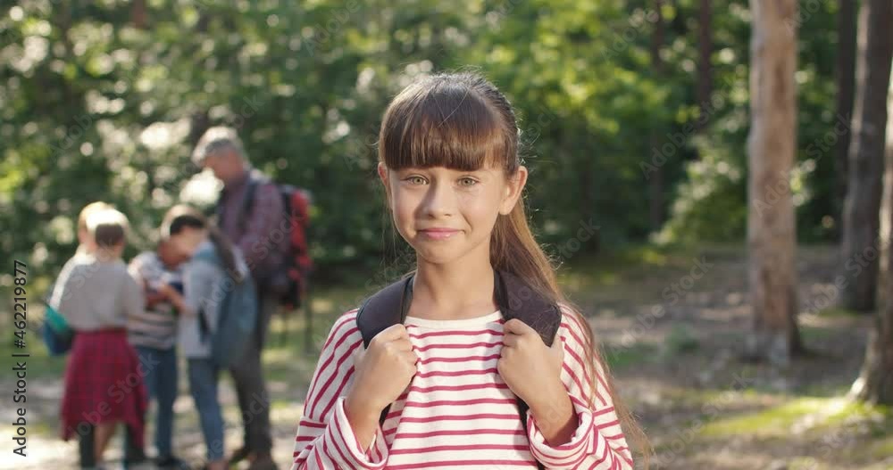 Portrait of little caucasian girl standing in wood. Good looking female kid posing to camera and smiling. Close up of beautiful child with long hair in park with smile on her face Portrait of little caucasian girl standing in wood. Good looking female kid posing to camera and smiling. Close up of beautiful child with long hair in park with smile on her face