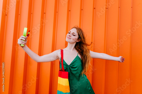 Woman using handheld motorized fan standing in front of orange wall photo