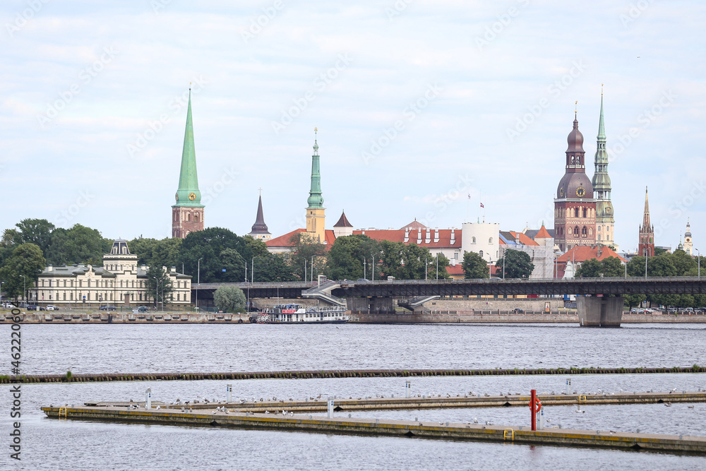 Obraz premium Cityscape view of Old Riga house and church towers in background and yach pier in foreground.