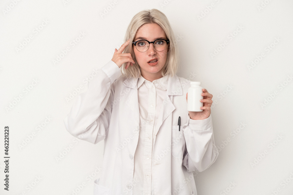 Young pharmacist woman holding pills isolated on white background showing a disappointment gesture with forefinger. Young pharmacist woman holding pills isolated on white background showing a disappointment gesture with forefinger.